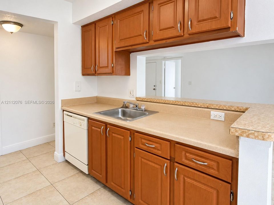 Kitchen featuring stained wood cabinetry, stone-finish countertops, stainless steel sink with metal faucet, integrated dishwasher, and tiled flooring