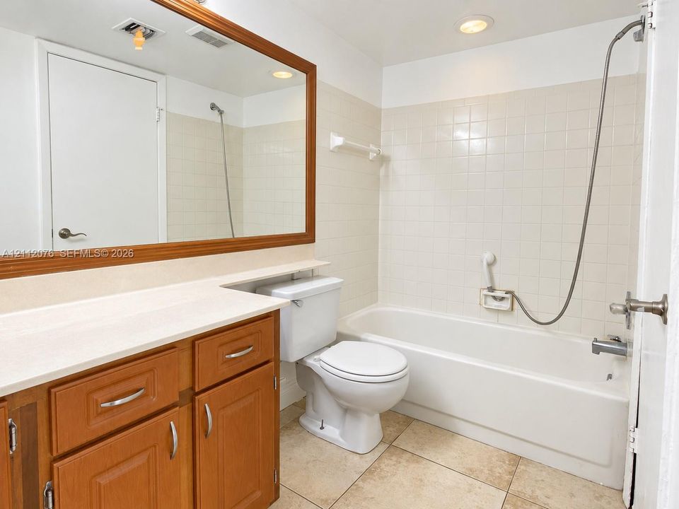 Bathroom featuring a wood-toned vanity with an integrated countertop, a full-width mirror with a wood frame, tile flooring, and a shower-tub combination with wall-mounted tiled surround