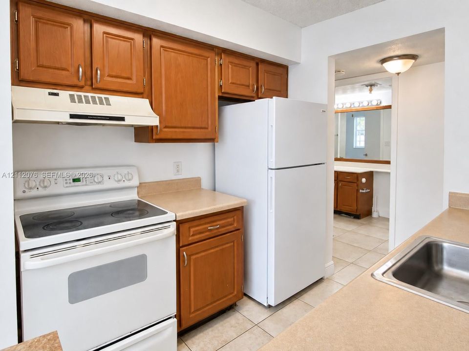 Kitchen featuring stained-wood cabinetry, white appliances, a solid-surface countertop, an inset stainless steel sink, and tile flooring