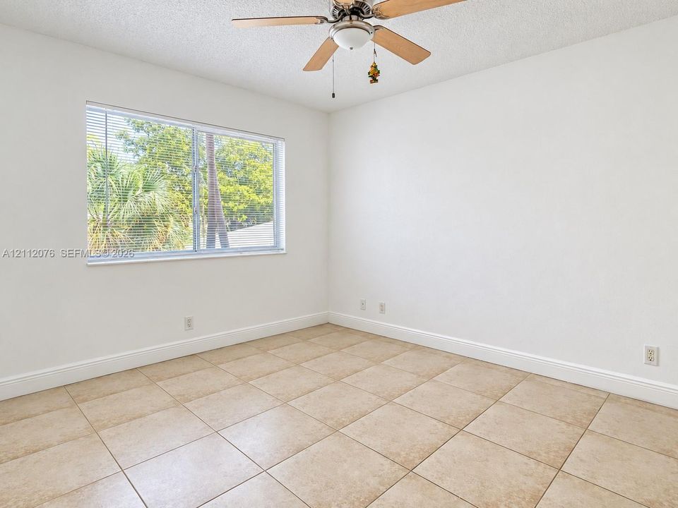 Neutral-toned ceramic tile flooring, clean white wall finishes, a multi-pane window with horizontal blinds, and a central ceiling fan with integrated lighting