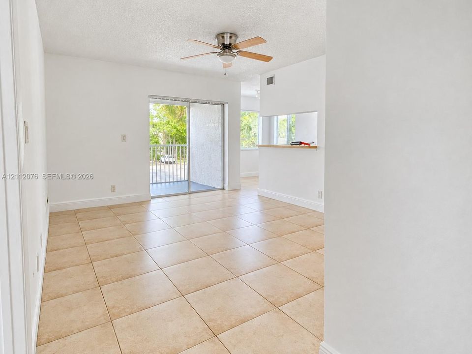 Neutral tile flooring, ceiling fan with light fixture, and sliding glass door opening to a balcony