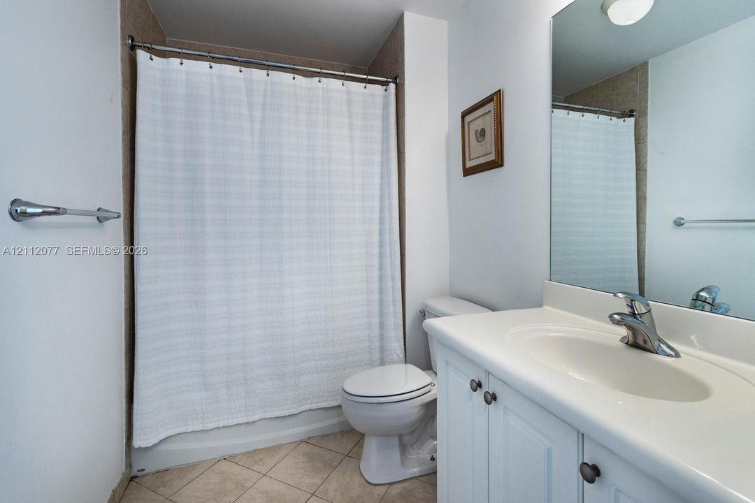 Bathroom featuring a white vanity cabinet with an integrated sink, a large wall-mounted mirror, ceramic tile flooring, and a shower-tub combination