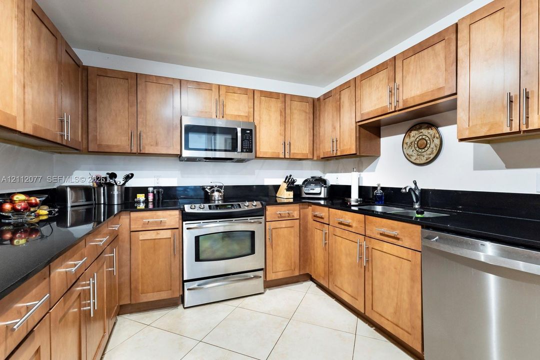 Kitchen featuring flat-panel wood cabinetry, black solid-surface countertops, stainless steel appliances, and diagonal tile flooring