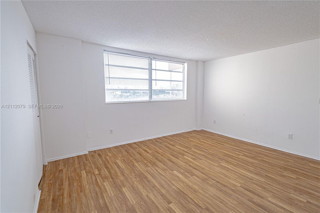 Room featuring wood-finish flooring, white walls, and a large multi-pane window with louvered blinds