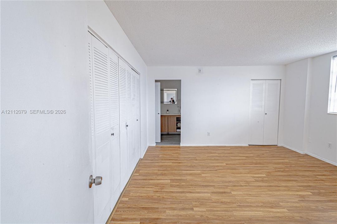 Wood-finish flooring, two sets of white louvered-door closets, and an entryway leading to a separate area with wood-finish cabinetry