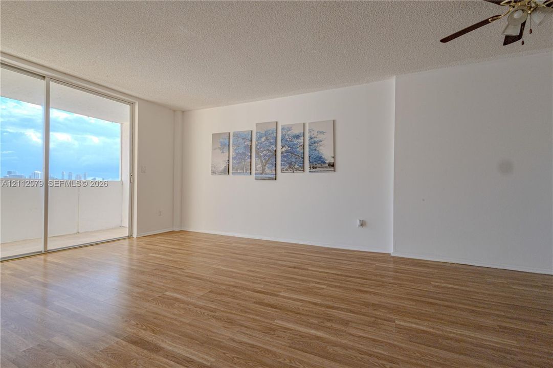 Open interior space featuring wood-finish flooring, textured ceiling, ceiling fan, and sliding glass doors with access to an exterior balcony