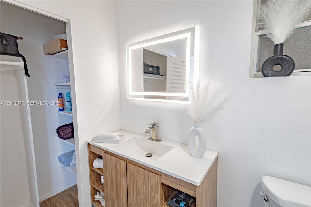 Modern vanity with wood-finish cabinetry, integrated countertop sink, LED-backlit mirror, and brushed-finish faucet