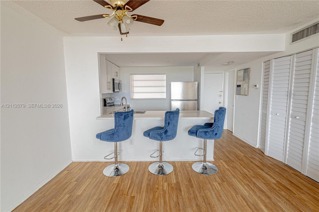 Kitchen featuring a breakfast bar, stainless steel appliances, white cabinetry, wood-finish flooring, and louvered closet doors