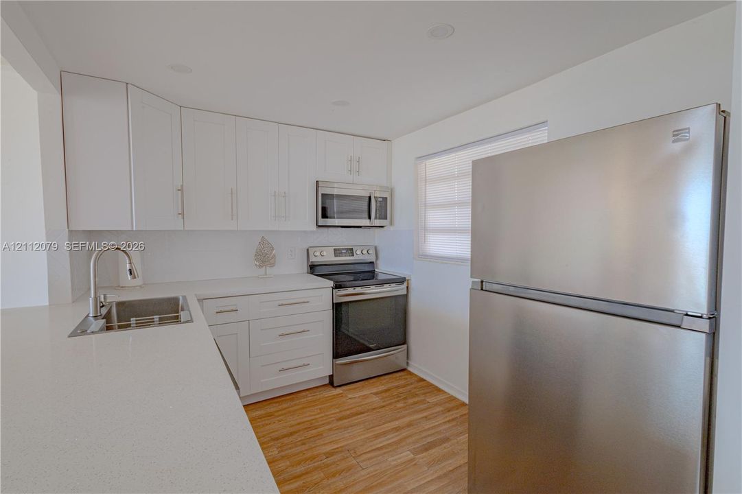 Kitchen featuring white shaker cabinetry, solid-surface countertops, stainless steel appliances, and wood-finish flooring