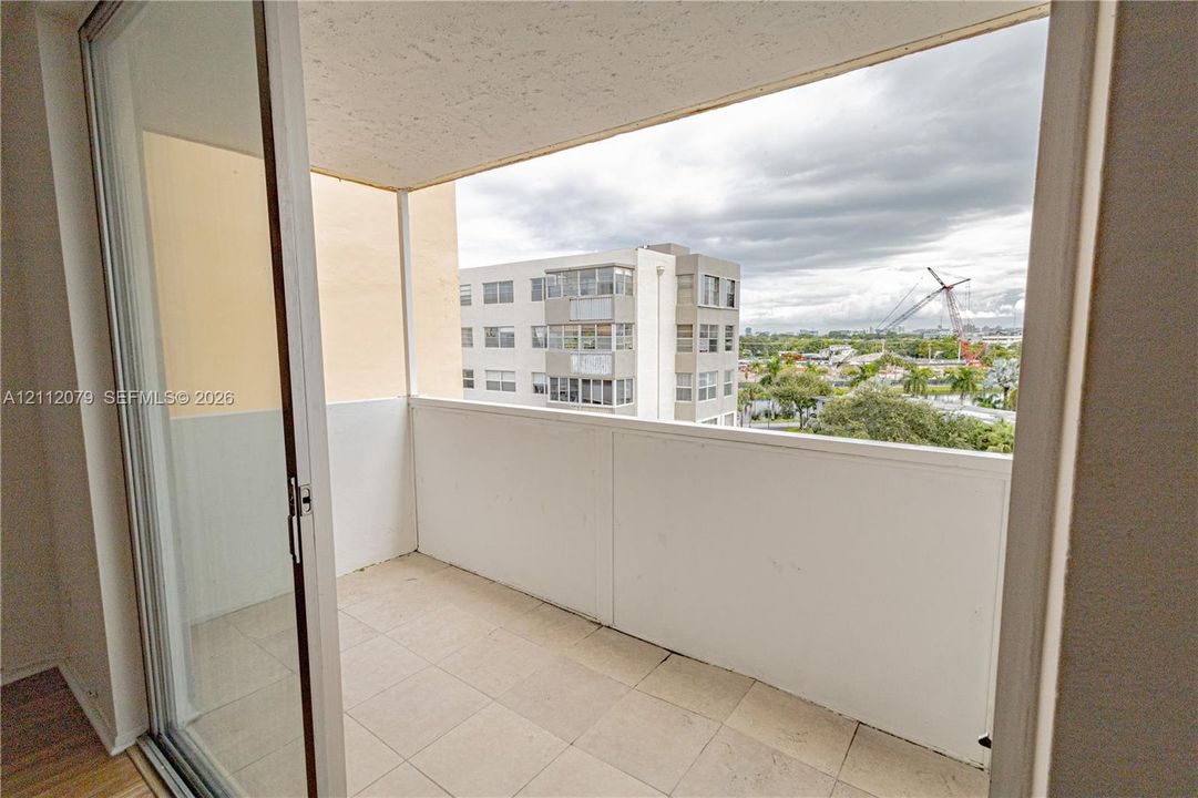 Covered balcony featuring tile flooring and a solid perimeter wall, accessed through a sliding glass door