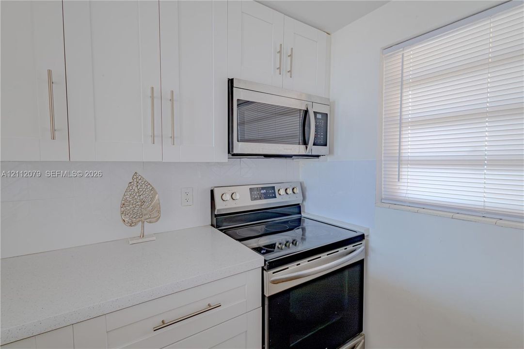 Kitchen featuring white shaker-style cabinetry, solid-surface countertops, a stainless steel electric range, a stainless steel over-the-range microwave, and horizontal blinds
