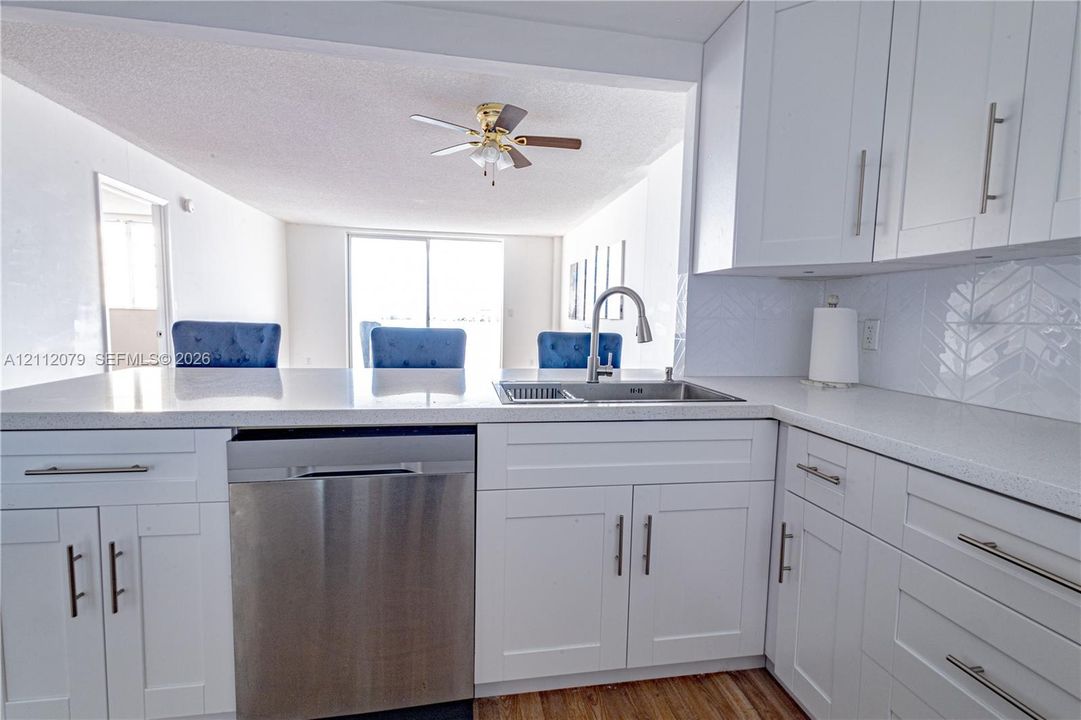 White cabinetry with bar-style hardware, stone-composite countertops, stainless steel undermount sink, herringbone-patterned tile backsplash, and stainless steel dishwasher