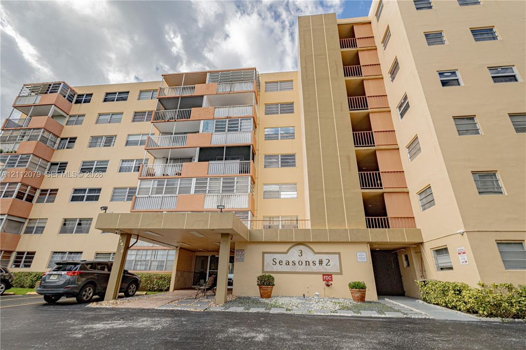 Mid-rise residential building exterior featuring a covered porte-cochère, multi-level private balconies, and horizontal jalousie windows