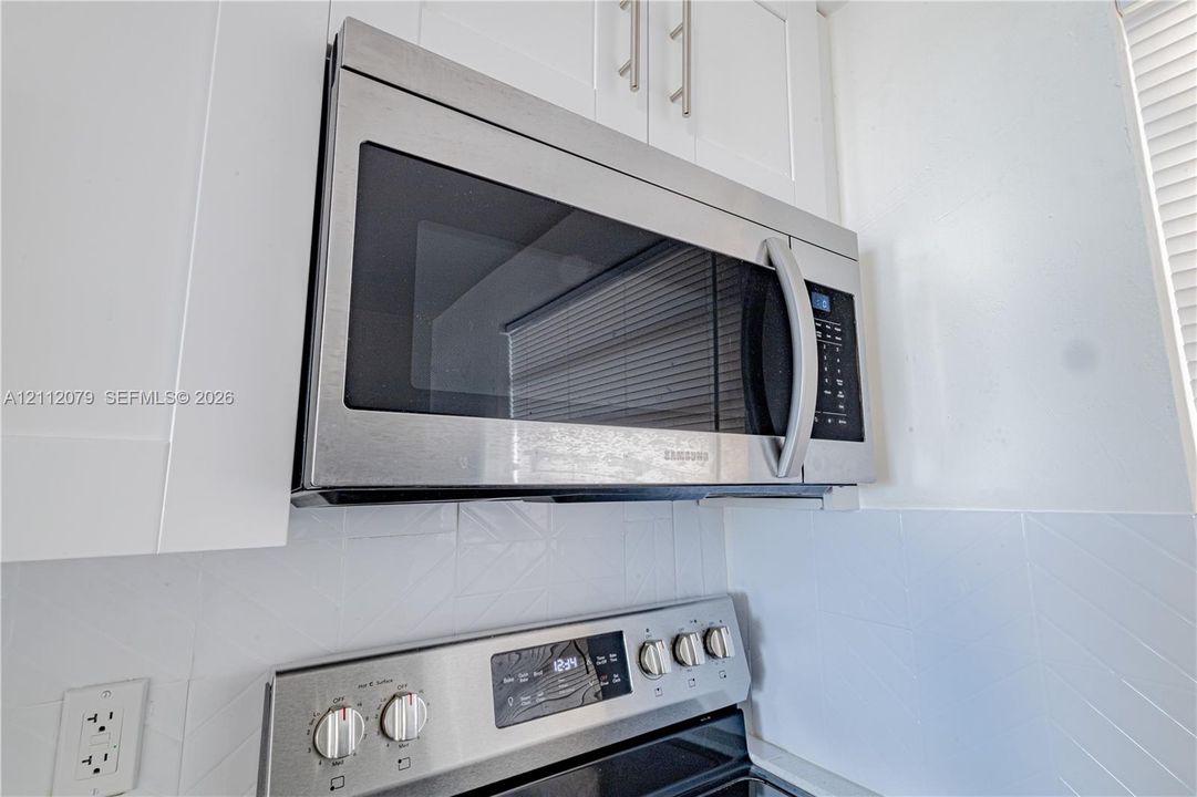 Stainless steel over-the-range microwave, white shaker-style cabinetry, and white tiled backsplash