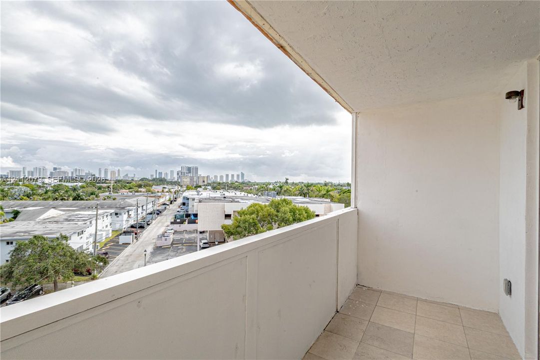Covered balcony featuring tile flooring, solid wall railings, and a wall-mounted light fixture, offering a cityscape panorama