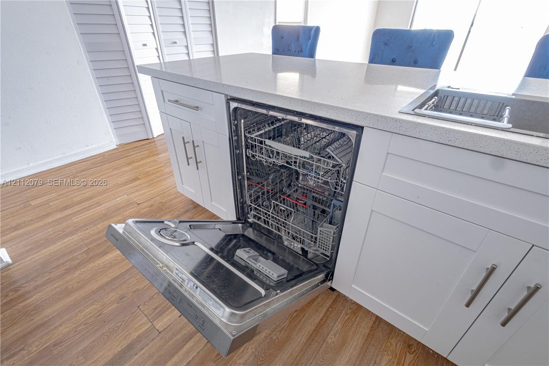 Kitchen island featuring white shaker-style cabinetry, a light-toned solid surface countertop, stainless steel dishwasher, and wood-finish flooring