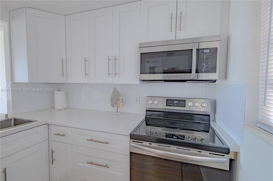 Kitchen featuring shaker-style white cabinetry, solid-surface countertops, stainless steel electric range, built-in stainless steel microwave, and herringbone-patterned tile backsplash