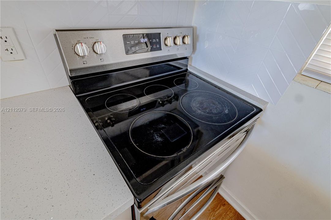 Stainless steel electric range featuring a flat glass cooktop and solid-surface countertop with a white herringbone tile backsplash