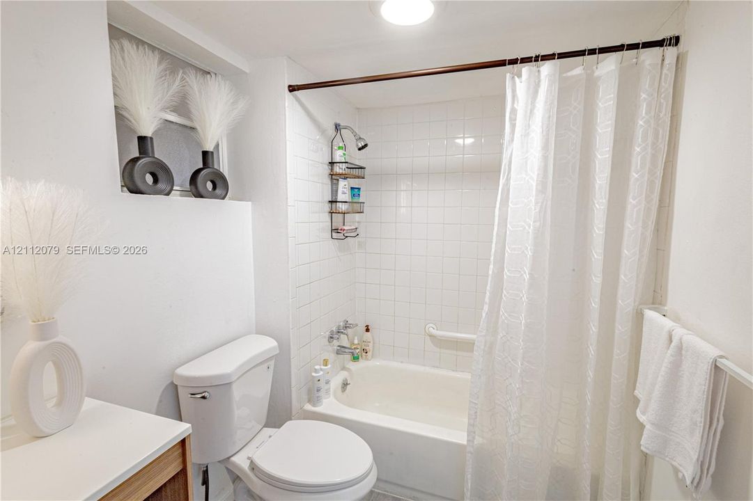 Bathroom featuring a bathtub with a tiled surround, a mounted grab bar, a wall-mounted shower head, and a vanity with a white countertop
