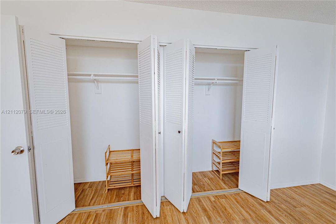 Dual closets featuring white louvered bifold doors and built-in upper shelving, complemented by wood-finish flooring