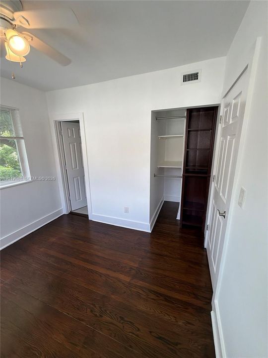 Wood-finish flooring, ceiling fan with integrated light fixture, and closet featuring built-in shelving