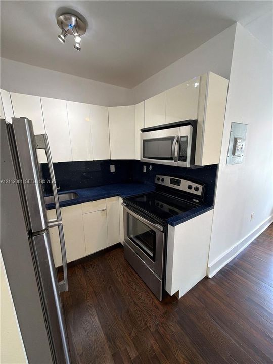 Kitchen featuring gloss-finish cabinetry, dark solid-surface countertops, stainless steel appliances, wood-finish flooring, and multi-directional track lighting