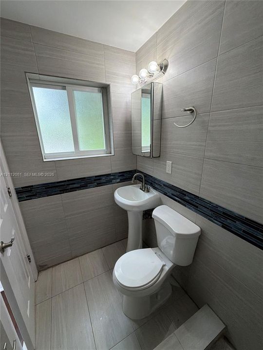 Pedestal sink with a polished metal faucet, built-in medicine cabinet, ceramic tile flooring, and floor-to-ceiling tile walls with a decorative glass accent border