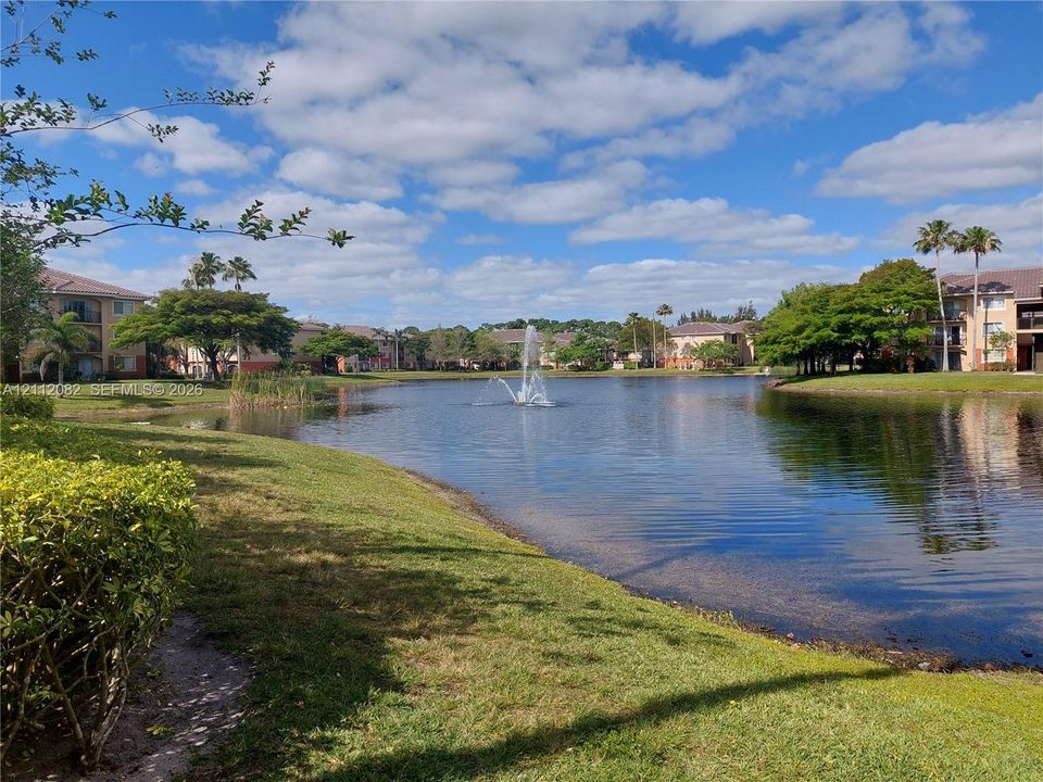 Community pond featuring a central fountain, manicured lawn, and mature trees