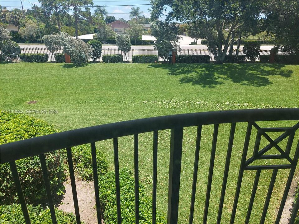 Black metal balcony railing overlooking a manicured lawn, established landscaping, and perimeter fencing