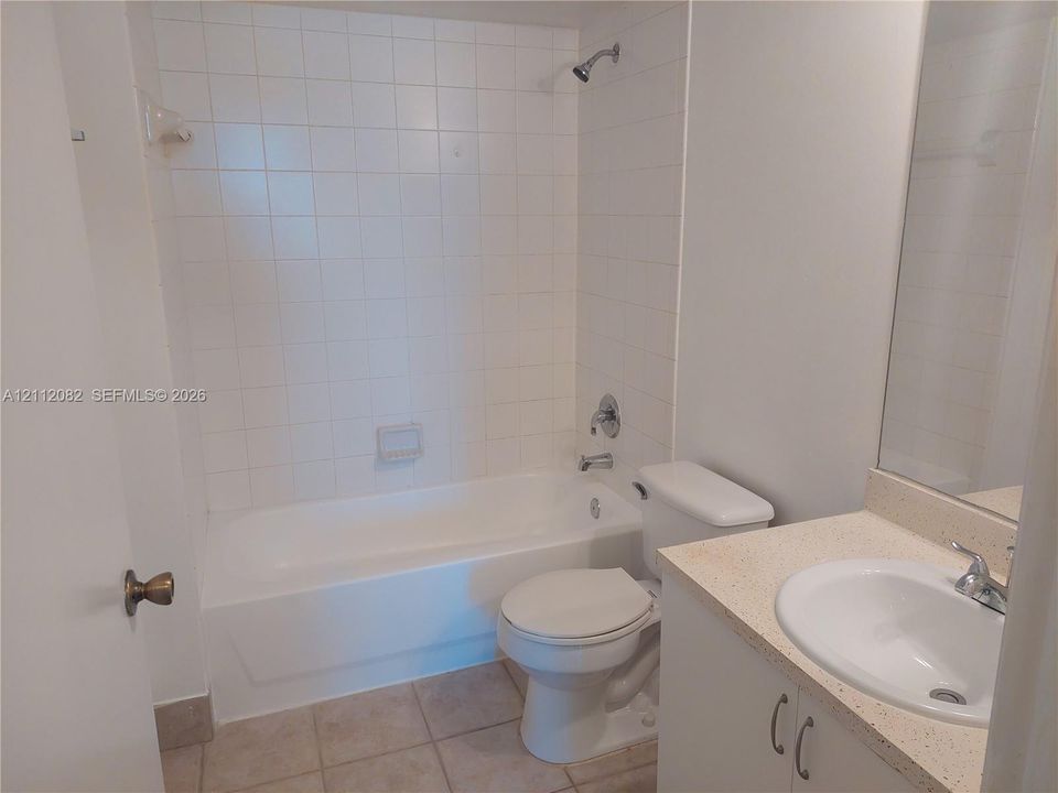 Bathroom featuring a white vanity with a solid-surface countertop, an integrated sink, floor-to-ceiling ceramic wall tile surrounding the bathtub, and neutral tile flooring