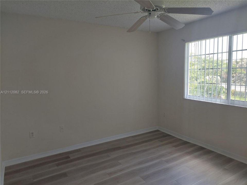 Room featuring wood-finish flooring, a multi-blade ceiling fan, and a window with security bars