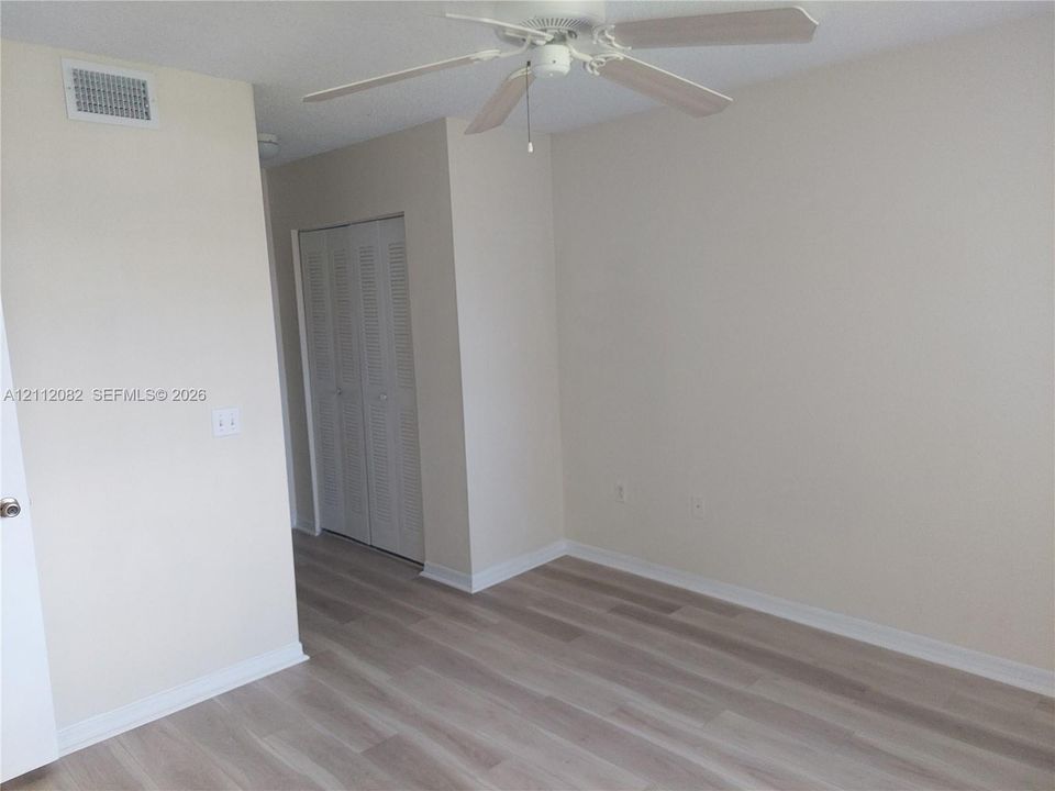 Neutral-toned interior featuring wood-finish flooring, a ceiling fan with light fixture, and louvered closet doors