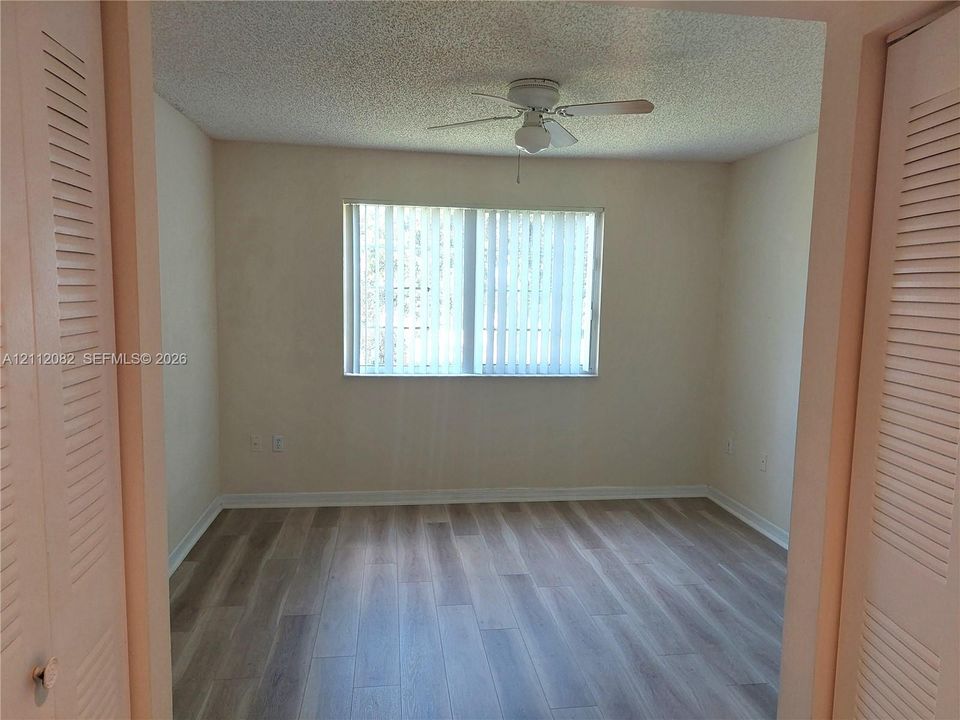 Wood-finish flooring, ceiling fan with integrated light fixture, window with vertical blinds, and dual bi-fold closet doors