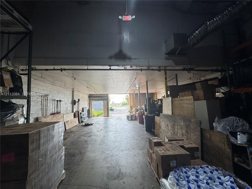 Industrial warehouse space featuring high ceilings, exposed brick walls, concrete flooring, and an open floor plan with rear access