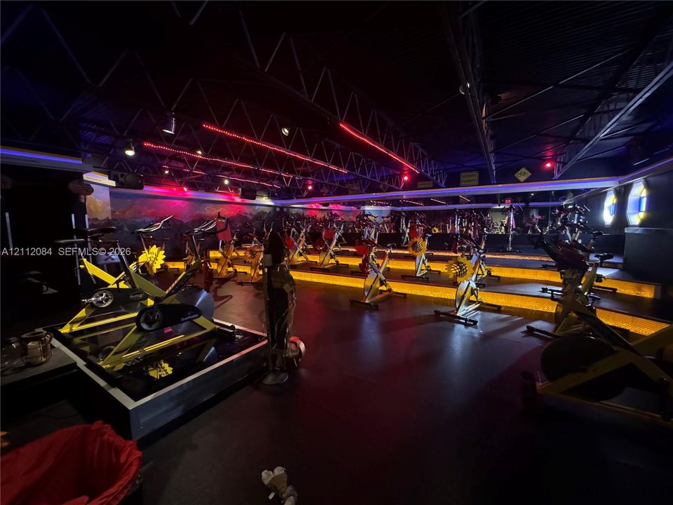 Multi-level exercise studio featuring tiered flooring, industrial-style exposed ceiling trusses, wall-to-wall mirrors, and built-in recessed platform lighting