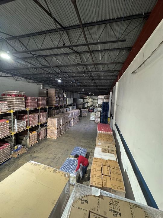 Industrial warehouse space featuring exposed steel truss ceiling, concrete flooring, and extensive metal racking systems