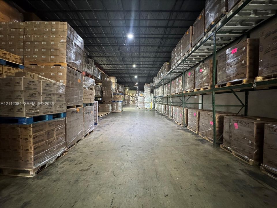 Industrial warehouse space featuring high ceilings with exposed structural steel, heavy-duty multi-level racking systems, polished concrete flooring, and overhead lighting