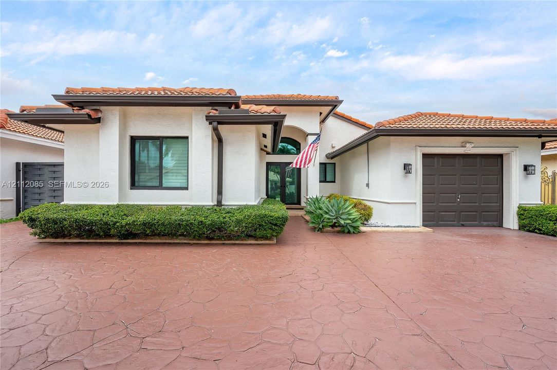 Stucco exterior residence featuring a terracotta-tiled roof, stamped concrete driveway, and attached garage