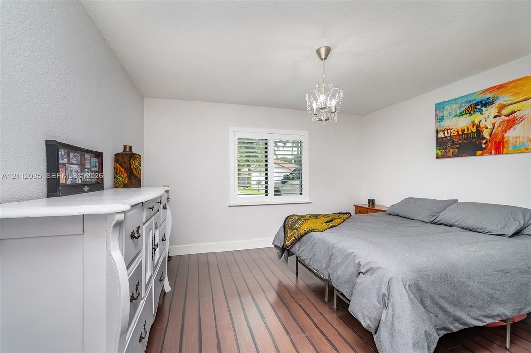 Room interior featuring wood-finish flooring, plantation shutters, and a crystal-style chandelier