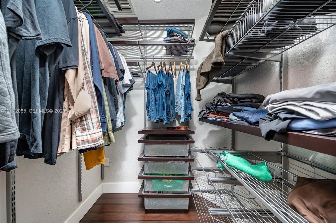 Walk-in closet featuring adjustable wire shelving, integrated hanging rods, built-in drawer units with clear storage bins, and dark wood-finish flooring