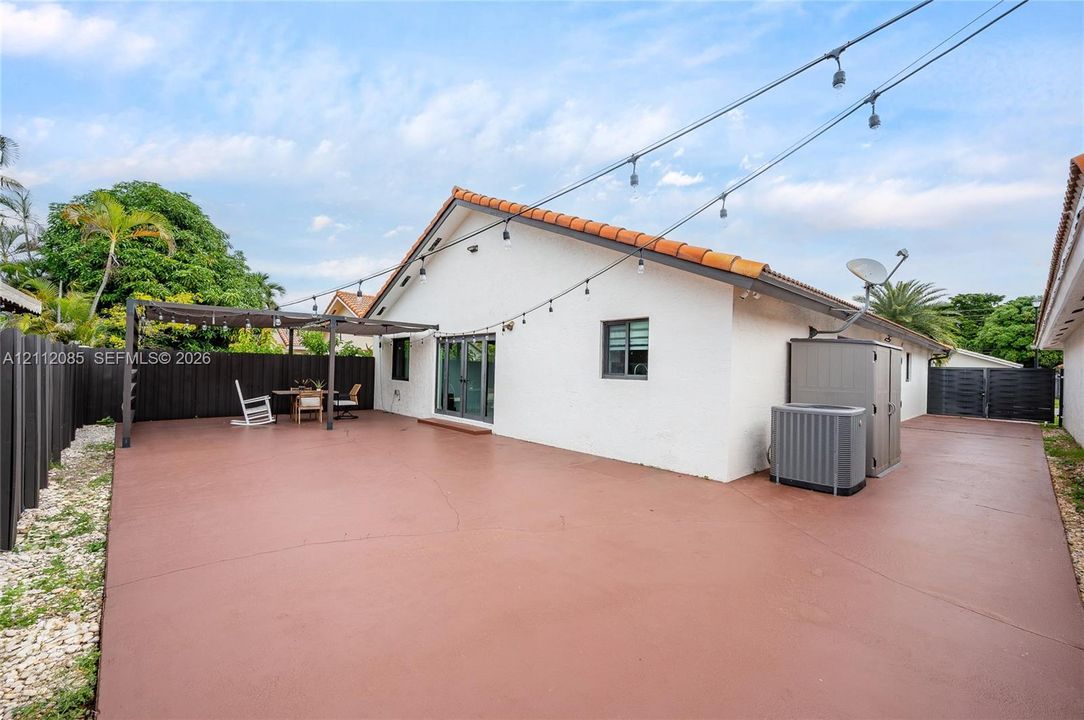 Rear exterior featuring a concrete patio, terracotta roof tiles, stucco siding, and a metal-frame pergola