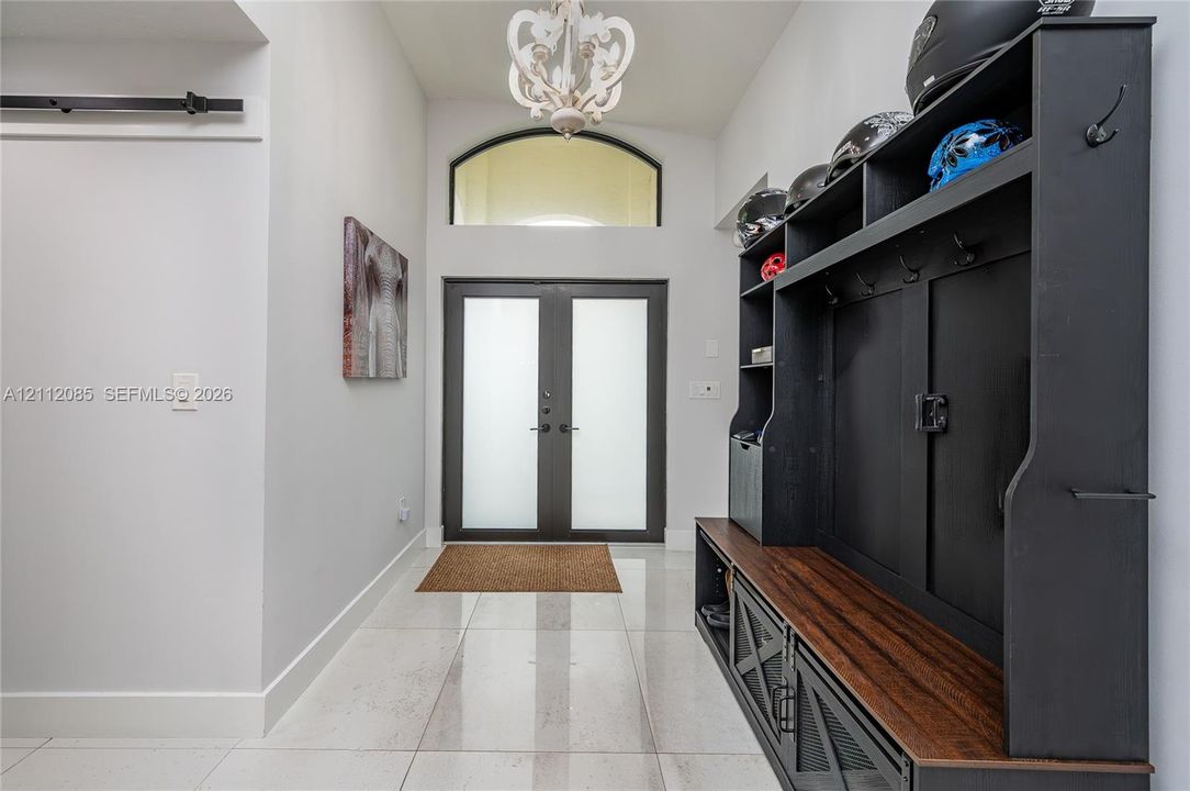 Double front entry doors featuring frosted glass panels, arched transom window, polished tile flooring, and decorative hanging light fixture