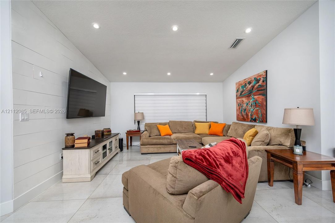 Living area featuring large-format tile flooring, recessed ceiling lighting, and a horizontal shiplap accent wall