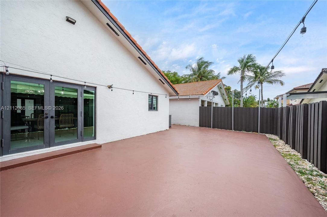 Expansive concrete patio featuring dual glass-panel doors, low-maintenance gravel landscaping, and vertical privacy fencing