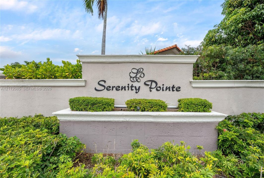 Stucco community signage with raised metal lettering, concrete cap details, and integrated landscaping featuring manicured shrubbery