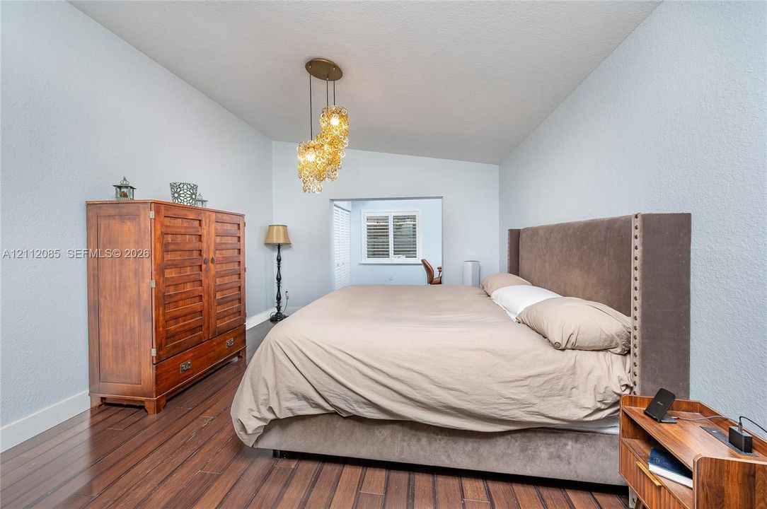 High-gloss wood-finish flooring, vaulted ceiling, multi-bulb amber glass chandelier, and window featuring plantation shutters