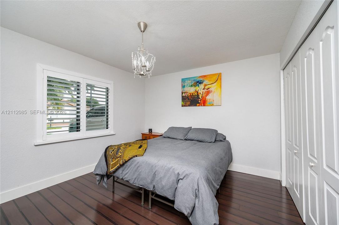 Room featuring wood-finish flooring, plantation shutters, multi-paneled sliding closet doors, and a decorative crystal-style chandelier