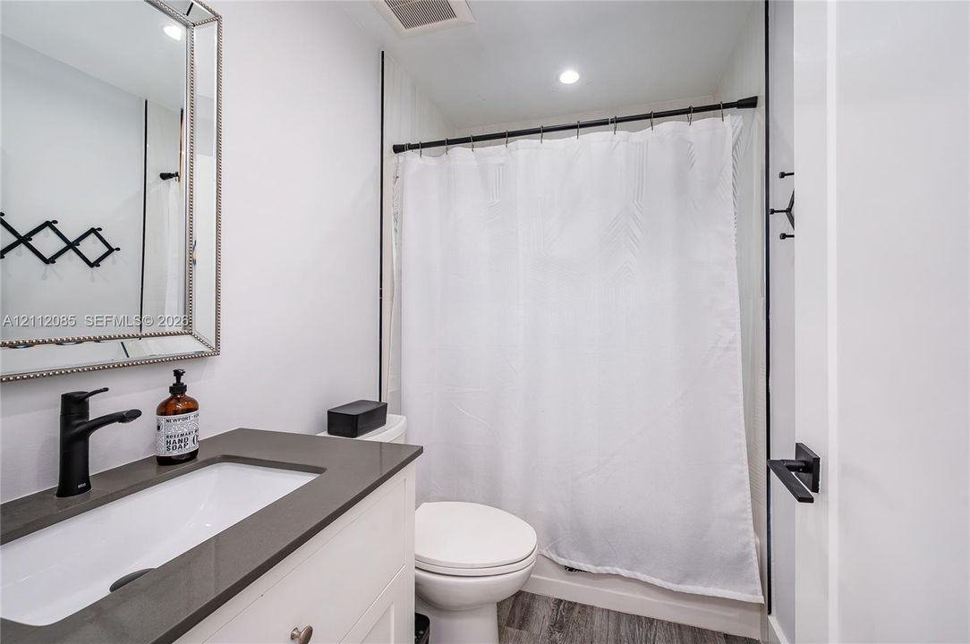 Bathroom featuring a white cabinet vanity with a solid-surface countertop, rectangular undermount sink, matte black faucet, and a framed mirror