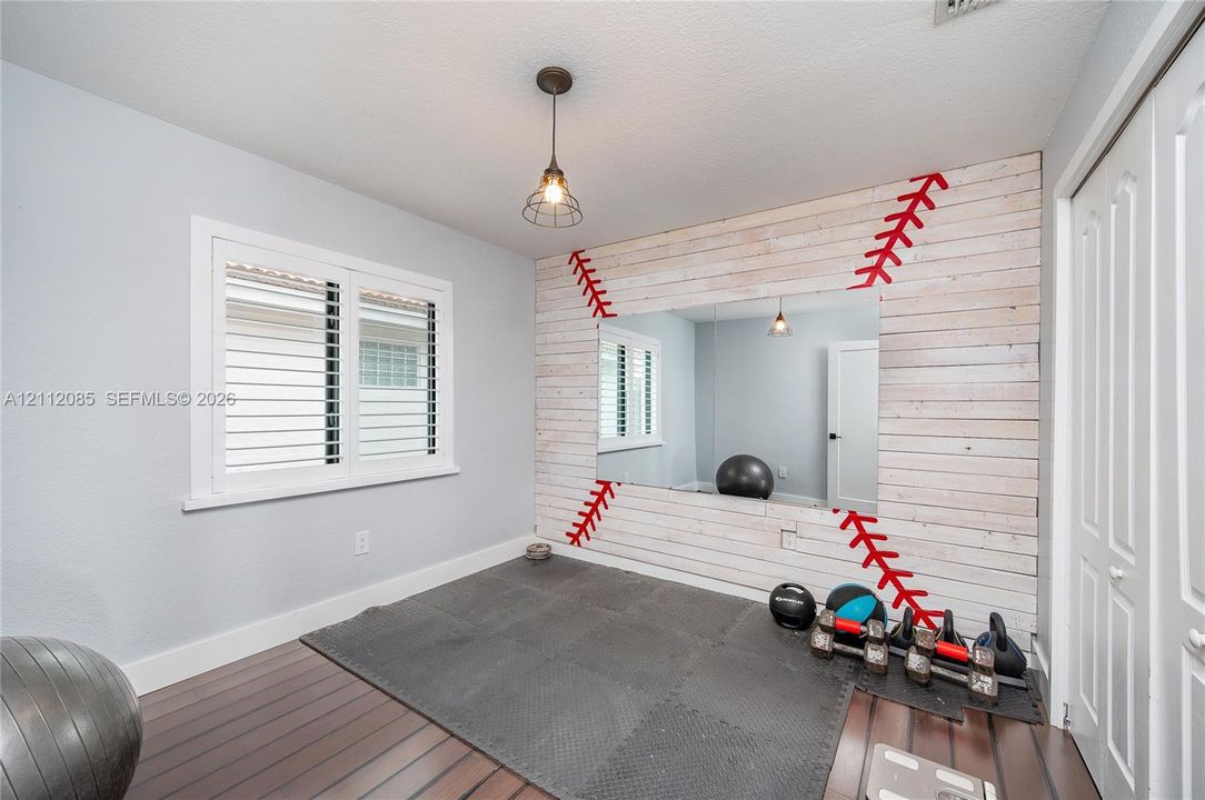 Room featuring wood-finish flooring, white plantation shutters, a decorative horizontal wood-plank accent wall with an integrated rectangular mirror, and a modern industrial pendant light fixture