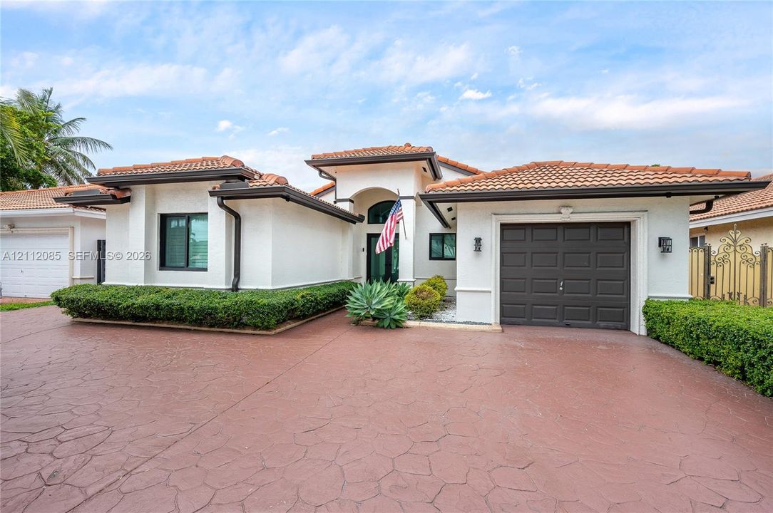 Stucco exterior featuring a clay tile roof, expansive stamped concrete driveway, and attached garage